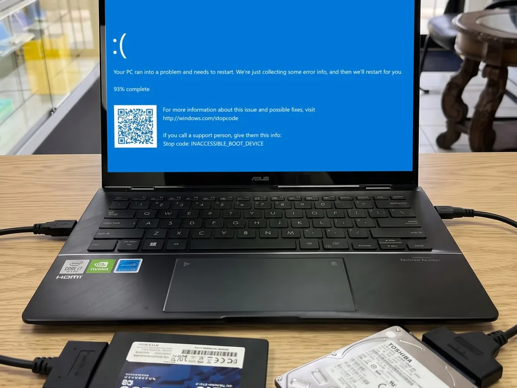Laptop ASUS con la pantalla azul INACCESSIBLE_BOOT_DEVICE junto a un SSD de 256GB y un disco duro Toshiba con adaptadores USB