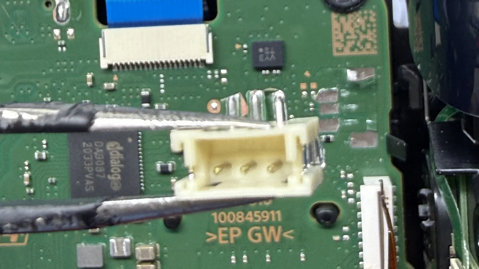 Battery connector ripped off a PS5 DualSense controller board, held in tweezers above the damaged pads