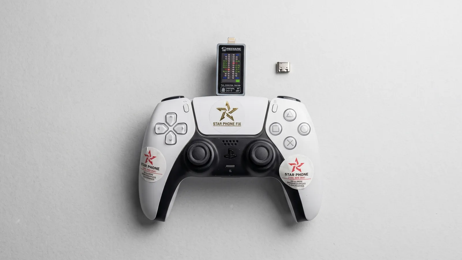PS5 DualSense controller with a USB-C power tester plugged in and a replacement USB-C charging port beside it