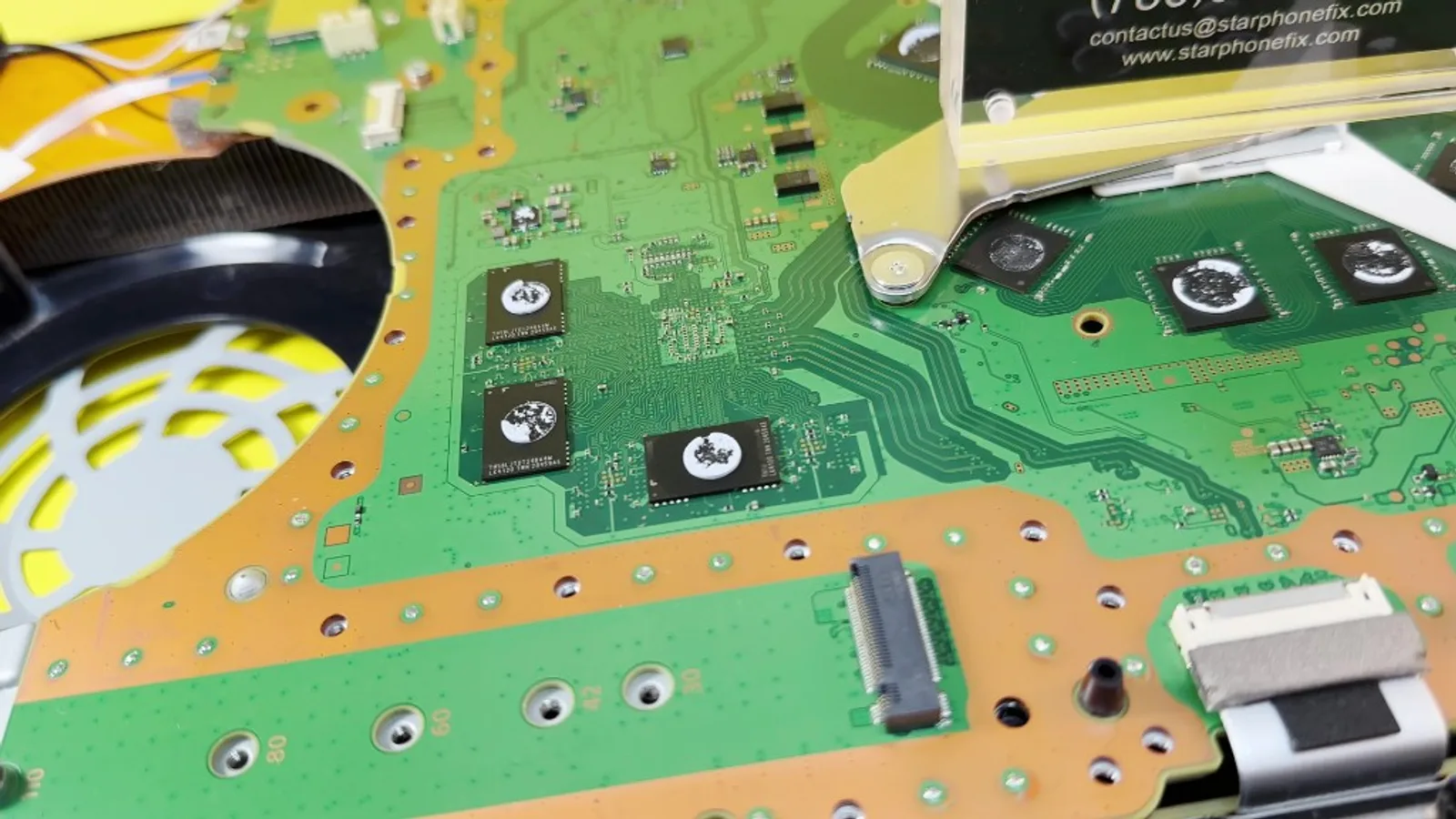 PlayStation 5 motherboard on the repair bench with thermal compound on chips and cooling fan nearby