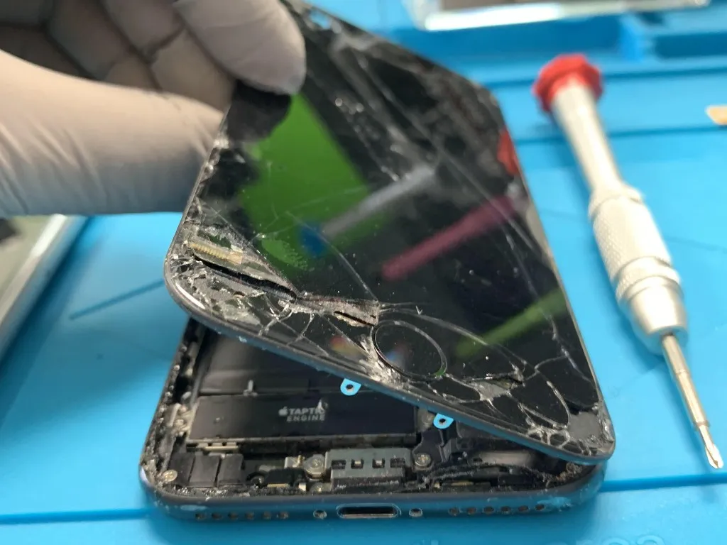 Technician lifting a shattered iPhone screen away from the phone's internal components during a repair