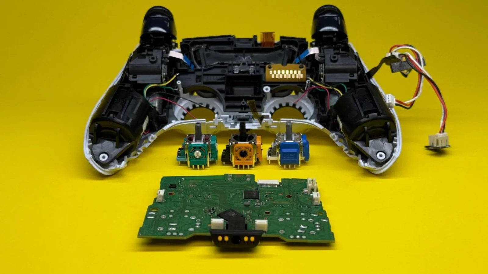 Disassembled controller with potentiometer, Hall Effect, and TMR joystick modules on a yellow background