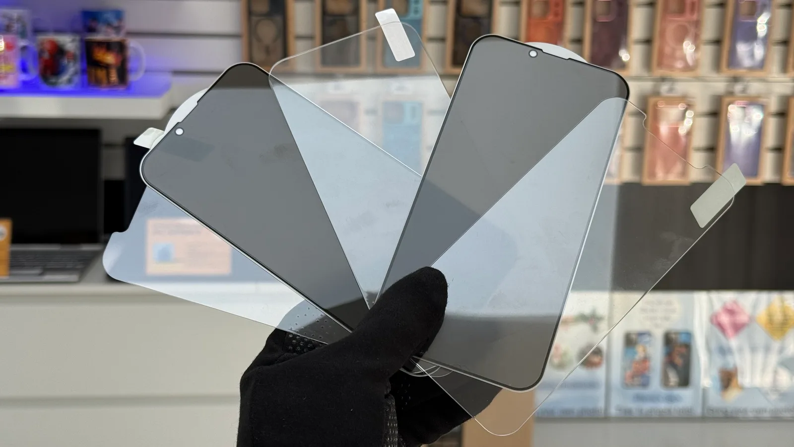 Hand holding several tempered glass screen protectors in clear and privacy versions inside a phone accessories store