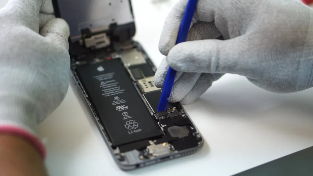 Technician using a blue pry tool on an opened iPhone during professional repair