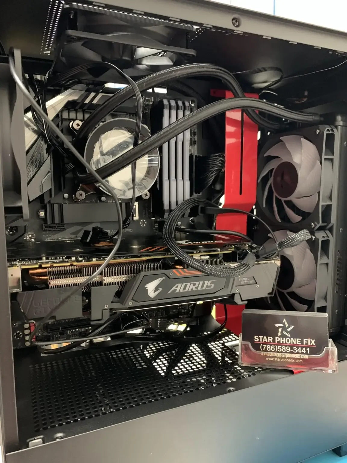 Interior of an open desktop computer tower with graphics card, cooling fans, and a Star Phone Fix business card