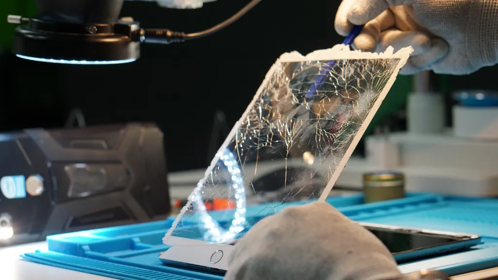 Technician lifting a shattered iPad screen during tablet repair under a ring light